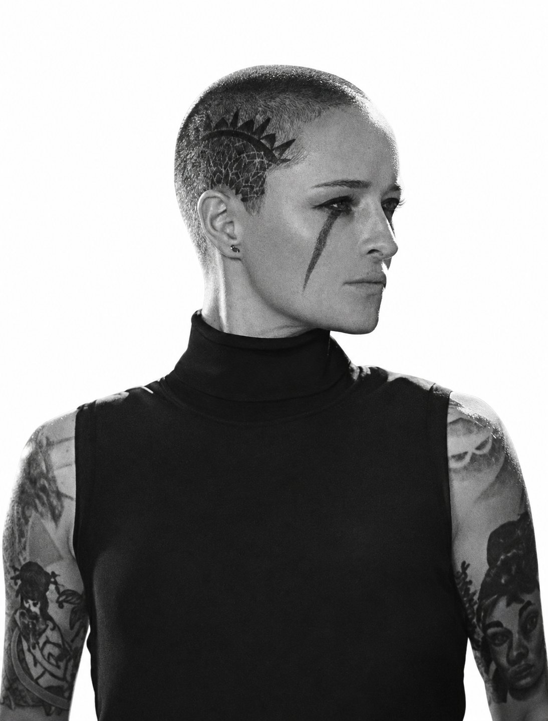 A woman in a black turtleneck with a tattoo running from her eye down her cheek — a literal malar stripe